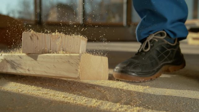 SLOW MOTION, CLOSE UP, DOF: Clumsy contractor cutting wood almost drops a wooden beam on his foot. Unrecognizable man working at a busy construction site almost drops a heavy plank on his foot.
