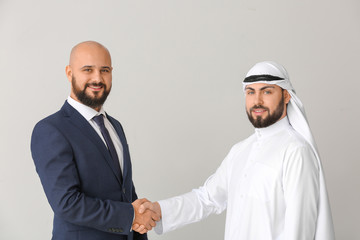 Fototapeta premium Arab man and his business partner shaking hands on grey background