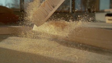 SLOW MOTION, CLOSE UP, DOF: Heavy wood beam covered in sawdust falls on the ground at a busy construction site. Pieces of timber fall on the ground after being cut up by a contractor's chainsaw.