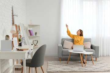 Young woman switching on air conditioner at home