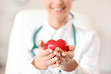 Female cardiologist with red heart in modern clinic, closeup