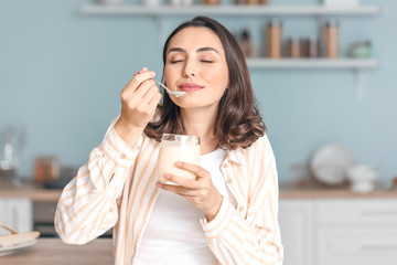 Young woman eating tasty yogurt at home