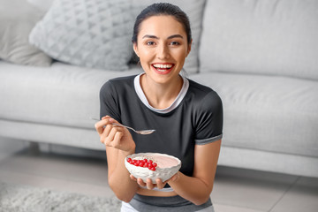 Young woman eating tasty yogurt at home