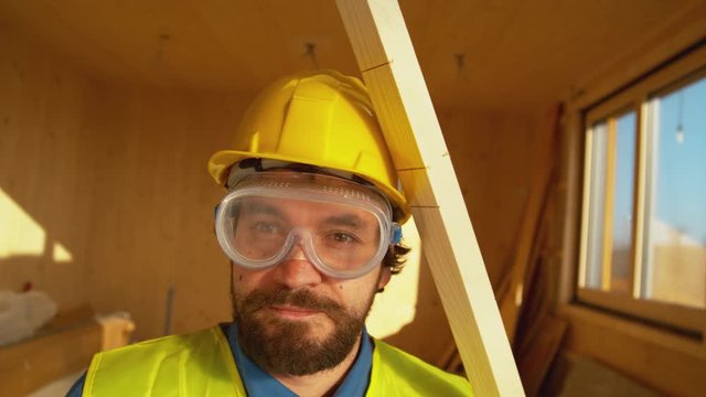 SLOW MOTION, CLOSE UP, PORTRAIT: Small plank falls from above on an unsuspecting contractor's head. Wooden board falls on a worker's head. Yellow hard hat saves Caucasian builder's from a concussion.