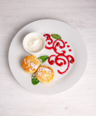 Cottage cheese pancakes or cheesecakes with sour cream on a white ceramic plate are decorated with jam. Delicious Breakfast or brunch. Menu
