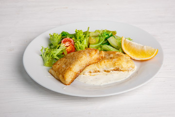 a piece of fried fish with salad leaves on a light background of the menu