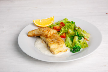 a piece of fried fish with salad leaves on a light background of the menu
