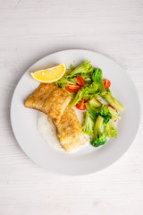 a piece of fried fish with salad leaves on a light background of the menu