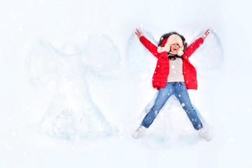 Fototapeta na wymiar Snow angel concept. Happy woman enjoying first snow, lying in snow and making snow angel.
