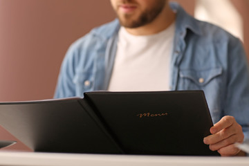 Young man with menu sitting in restaurant, closeup