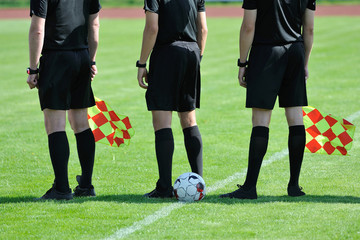 three football referees with flags and a ball before the match