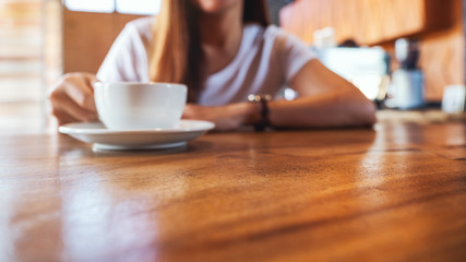 Closeup image of a woman holding a cup of hot coffee on wooden table