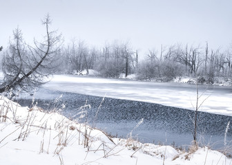 Snowy winter landscape in the open countryside with a half frozen lake.