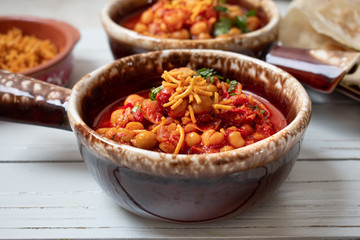 Indian garbanzo beans curry served in clay pots on white wooden background