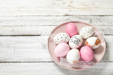Beautiful easter eggs in a plate on a white wooden background, place for text, top view