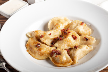 Dumplings and ravioli stuffed with meat. Sprinkle sliced smoked tomatoes. Served on a large white plate. Next to a bowl of sour cream. On a wooden background.