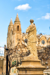 Vertical view of Balluta square in Sliema, Malta. Back of stone figure looking on Parish Church of Our Lady of Mount Carmel, or simply known as the Carmelite Church or Balluta Parish Church. Travel