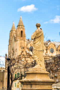 Vertical view of Balluta square in Sliema, Malta. Back of stone figure looking on Parish Church of Our Lady of Mount Carmel, or simply known as the Carmelite Church or Balluta Parish Church. Travel