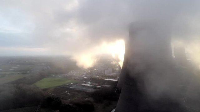Aerial view of atmospheric UK power station cooling towers through smoke steam emissions at sunrise.