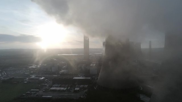 Aerial view of UK power station cooling towers smoke steam flying through emissions at sunrise.