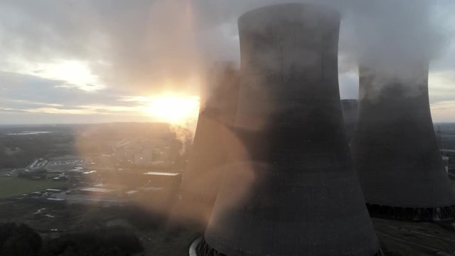 Aerial dolly right UK power station cooling towers smoke steam emissions, sunrise hiding behind chimney stack.