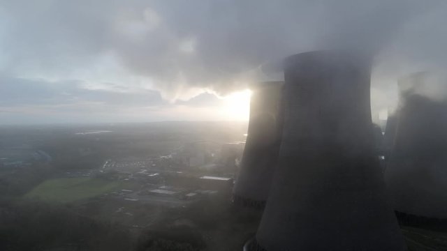 Aerial view of UK power station cooling towers dolly right through smoke steam emissions at sunrise.