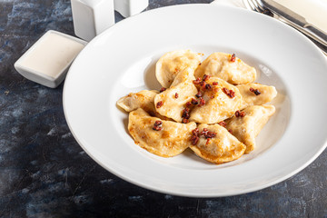 Dumplings and ravioli stuffed with meat. Sprinkle sliced smoked tomatoes. Served on a large white plate. Next to a bowl of sour cream. On a wooden background.