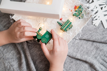 Hands of a child holding a gift, A wooden train toy is carrying New Year's gifts. On a cozy knitted gray sweater. top view