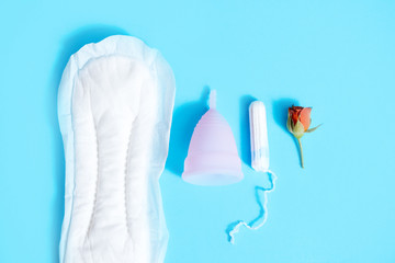 Feminine intimate hygiene set over blue background. Sanitary pad, swab or cup. the choice of a modern woman. Red rose. menstrual cycle concept in women