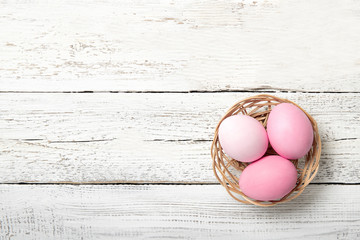 Easter eggs in a basket on a white wooden background, place for text, top view, isolation,