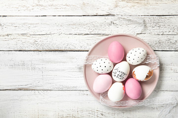 Beautiful easter eggs in a plate on a white wooden background, place for text, top view