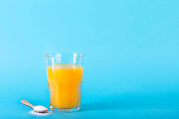 A glass juice and a spoon with collagen powder on blue background.