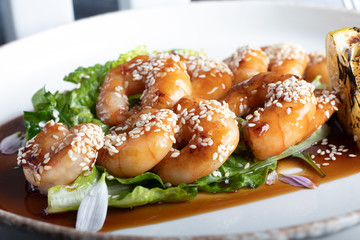 Shrimps cooked in teriyaki sauce with a slice of fried lemon on a pillow of lettuce leaves. On a white background, on a dark wooden background.