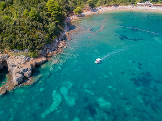 Aerial view of a steep cliff and a motor boat. Jagged coast on the Adriatic Sea. Cliffs overlooking the transparent sea. Wild nature and Mediterranean maquis. Mogren beach. Montenegro