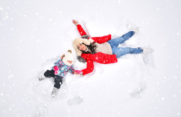 Mother and daughter enjoying first snow, lying in snow and making snow angel.