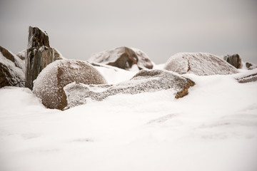 Frost-covered boulders in winter on a road with white snow, cloudy skies on a sunny winter day.