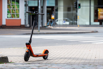 electric scooter or e-scooter parked on sidewalk, blurred city street background