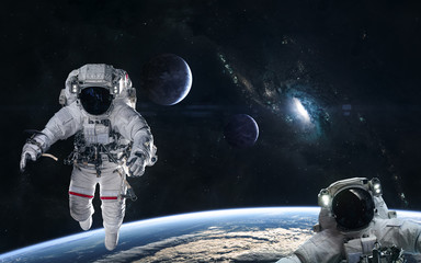 Astronauts in orbit of the planet on a background of blue spiral galaxy somewhere in deep space. Science fiction. Elements of this image furnished by NASA
