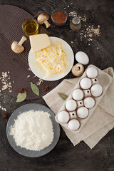 Ingredients for cooking, flour, eggs, grated cheese, mushrooms and spices, on a black background. Concept of making food, recipes.
