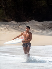 Young handsome man  wet all over body,walking on the beach,holding serf board righe side,show fit and firm muscle,reflection of sunlight shining on his skin