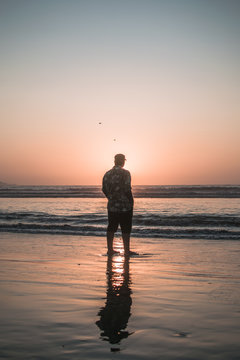 hombre parado en la orilla de la playa al atardecer