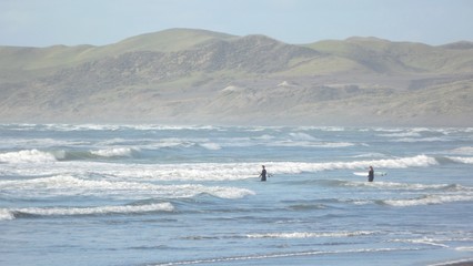 Two surfer with surf board Walking between the waves out in the Ocean, mountains in the background