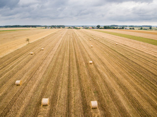 Aerial view of round hay bales on stubble with a village in the background