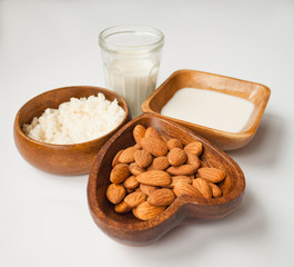 Homemade almond milk in a glass, almonds, milk and squeezed nut in wooden bowl on white background