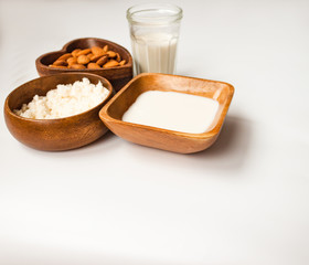 Homemade almond milk in a glass, almonds, milk and squeezed nut in wooden bowl on white background