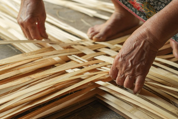 Hand elderly woman are weave bamboo strips of bottom of basket. - obrazy, fototapety, plakaty