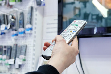 a person's hand presses the control buttons of the TV black remote at their leisure with their finger to change the lcd video channel
