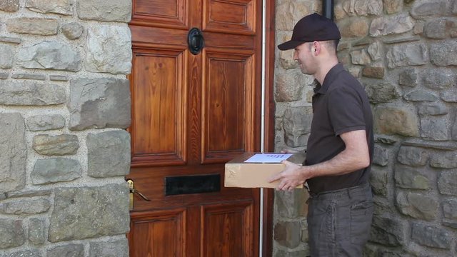 Courier / Delivery man delivering a parcel home delivery at a house. A woman open the front door and takes delivery of the package. Stock Video Clip Footage
