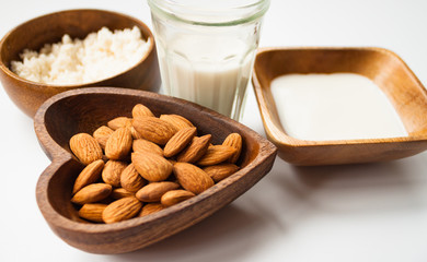 Homemade almond milk in a glass, almonds, milk and squeezed nut in wooden bowl on white background