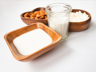 Homemade almond milk in a glass, almonds, milk and squeezed nut in wooden bowl on white background